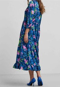 Květinové midi šaty v modré, zelené a růžové barvě s tříčtvrtečními rukávy, volánkovým lemem a lehkým materiálem. V kombinaci s modrými vysokými podpatky.