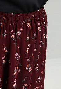 Falda floral burdeos con una textura suave, que presenta una cinturilla elástica y delicadas flores en tonos rosa, naranja y verde.