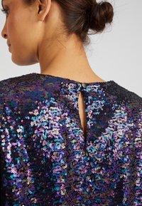 Sequined top in black with multi-colored sequins reflecting purple and blue hues, featuring a keyhole back and a button closure.