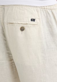 Lys beige linned shorts med en struktureret stof, der har en knaplukket baglomme og et lille mærke syet på linningen.