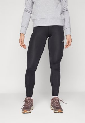 Czarne legginsy wykonane z elastycznego materiału, charakteryzujące się dopasowanym krojem i bezszwowym wzornictwem, zestawione z brązowymi butami sportowymi i szarym swetrem.