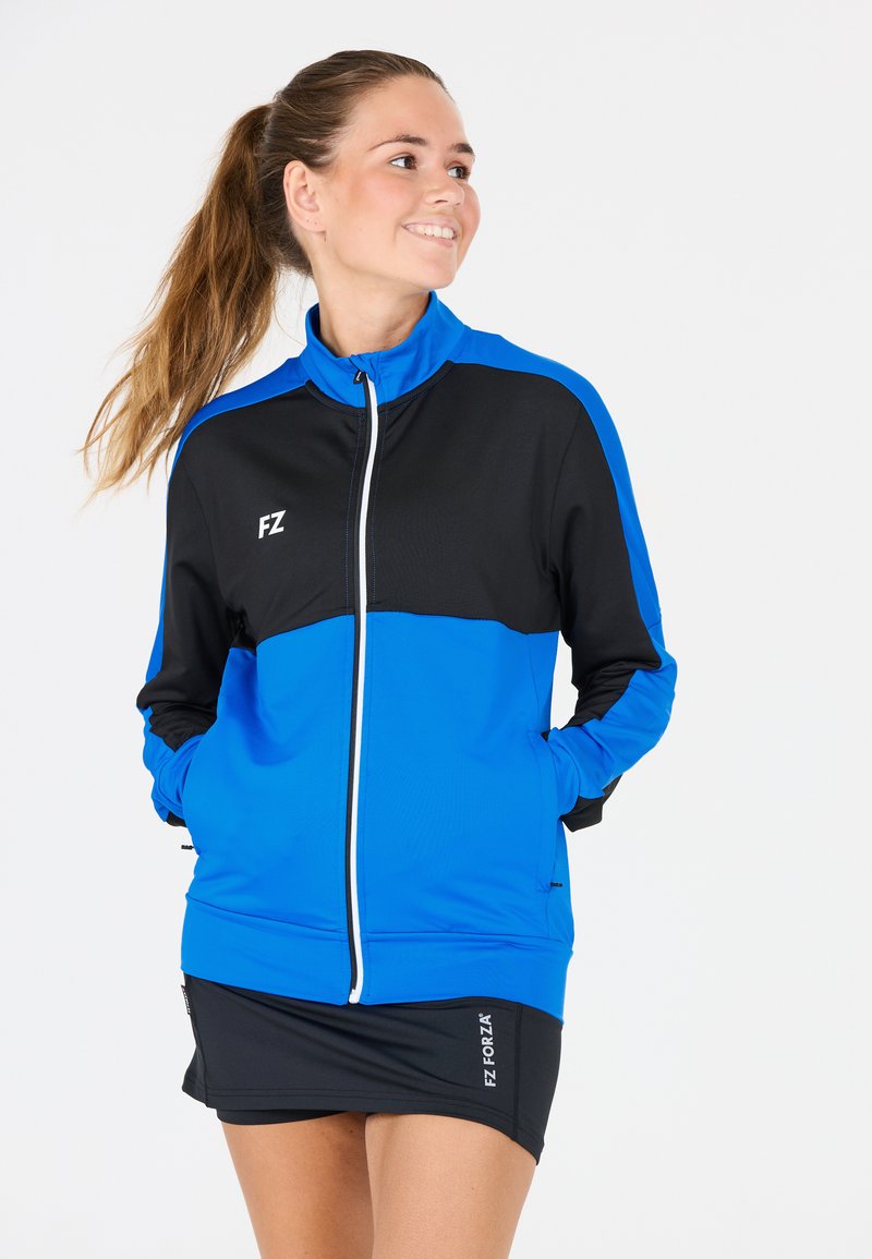 Kvinnors träningsjacka i blått och svart. Har dragkedja framtill, hög krage och sidofickor. Tillverkad av lätt, andningsbart material.