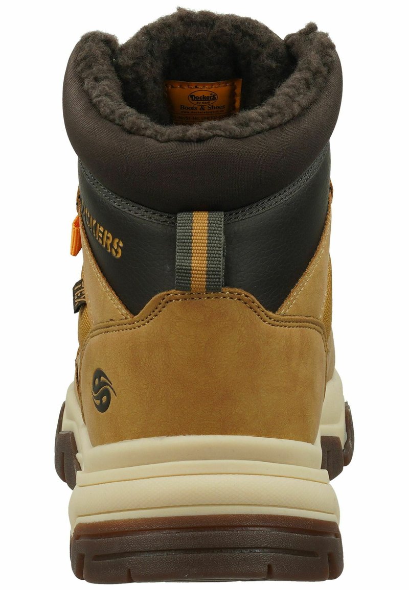 Bota de ante marrón y cuero negro con un cuello acolchado, acentos amarillos y una suela de goma texturizada. Presenta una cinta para tirar y un detalle del logo.