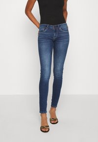 Smala denimjeans i mörk tvätt med en subtil blekningseffekt, med midjehög midja, fem fickor och dragkedja. Betonad med röd sömnad.