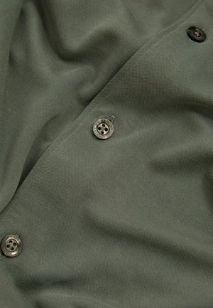 Țesătură de culoare verde măslinie cu un finisaj texturat, având butoane metalice rotunde și o cădere netedă. Amplasarea butoanelor pe margine accentuează designul.