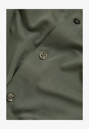 Olivgrüner Stoff mit texturierter Oberfläche, der runde, metallische Knöpfe und einen sanften Fall aufweist. Die Knopfplatzierung entlang des Randes betont das Design.