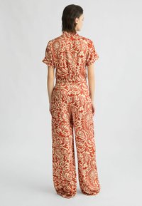 Rode en crèmekleurige jumpsuit met paisleypatroon, korte mouwen, ontspannen wijde pijpen en een elastische tailleband voor comfort.