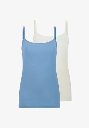 Junge Frau lächelt, trägt ein hellblaues Camisole und passende Unterwäsche, mit einem Arm über dem Kopf erhoben vor einem schlichten Hintergrund.