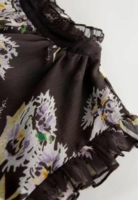 Fekete virágos blúz világoslila és sárga virágmintákkal, fodros nyakkivágással és lágy, áttetsző anyagtextúrával.