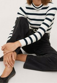 Pull à col roulé en tricot avec des rayures horizontales blanches et bleu marine, associé à un jean noir taille haute à jambe large et des chaussures plates noires.