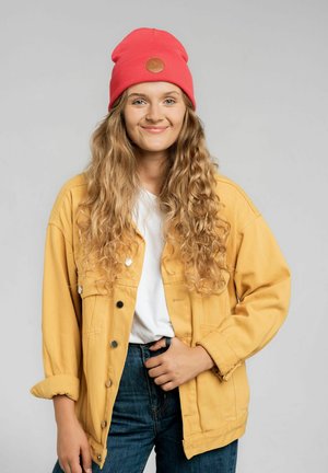 Czerwona wełniana czapka z dzianiny z skórzaną łatką logo, w połączeniu z żółtą dżinsową kurtką i białym t-shirtem, dopełniona ciemnoniebieskimi dżinsami.