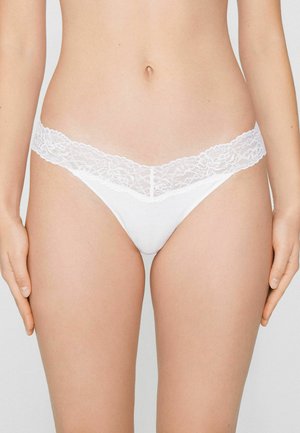String blanc avec une ceinture en dentelle. Le tissu est lisse et doux, avec un design minimaliste.