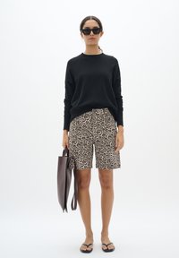 Pull noir, short en imprimé léopard en beige et marron, sac fourre-tout marron, tongs noires, lunettes de soleil noires surdimensionnées, coupe décontractée.