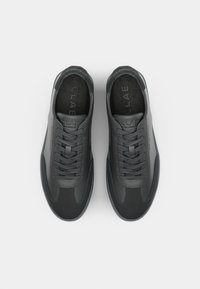 Black sneakers with a smooth leather and textile upper, featuring tone-on-tone laces and a textured insole with embossed logo.