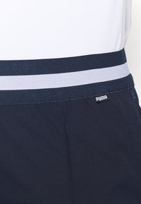 Marinblå byxor i texturerat tyg med grå resårmidja med kontrasterande färg och en logotypetikett, som framhäver en enkel och ren design.