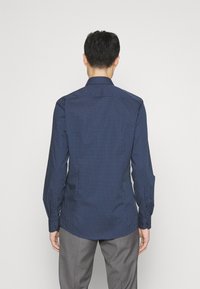 Granatowa koszula z długim rękawem z geometrycznym wzorem białych kropek, kołnierzykiem na guziki i dopasowanym krojem. Wykonana z gładkiej tkaniny.