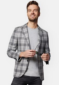 Szary marynarka w kratę w lekkim materiale, z klapami typu notch i zapięciem na guzik. Nosił ją na szarej koszulce, trzymając czarne okulary przeciwsłoneczne.