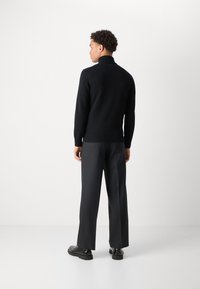 Pulover negru tricotat cu guler înalt, asociat cu pantaloni largi gri închis. Materialul pare moale; are mânici și tiv cu dantelă ribonată.