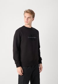 Zwarte crewneck sweatshirt met ribgebreide manchetten en onderkant. Kenmerkt zich door een prominent Calvin Klein Jeans-logo op de borst in contrasterende kleuren.