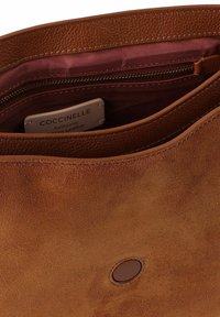 Braune Lederhandtasche mit weicher Textur, einem Reißverschluss im Inneren und einem Echtheitsanhänger. Außen mit einem abgerundeten Laschenakzent versehen.