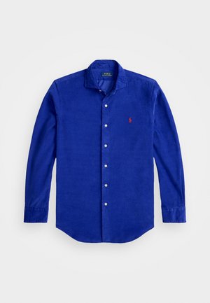 Camisa de pana de manga larga de color azul royal con botones blancos y un pequeño logo rojo bordado en el lado izquierdo del pecho.