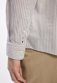 Gestreepte overhemd in grijs en witte katoen, met een knoopmanchet met twee knopen en een verstevigde plooi, gecombineerd met een beige stof eronder.