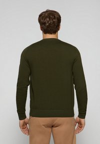 Mörkgrön stickad tröja med långa ärmar, rund hals och ribbade muddar. Slät textur, åtsittande design och en sömlös baksida.