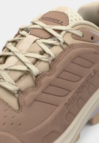 Beige vandrestøvle med struktureret stof og glatte detaljer. Har lys brune snørebånd, en polstret tunge og et udtalt mønster på sålen.