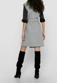 Vestito in misto lana grigio con maniche in velluto a coste nero e cintura in vita. Stivali alti fino al ginocchio in camoscio nero con tacco a punta completano il look.