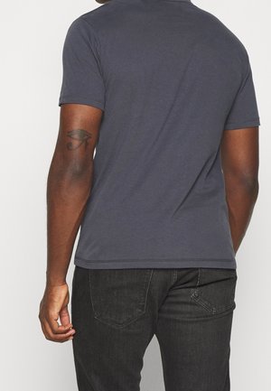 Dunkelgraues Baumwoll-T-Shirt mit kurzen Ärmeln, das über einen Rundhalsausschnitt und eine glatte Textur verfügt, getragen mit schwarzen Jeans.