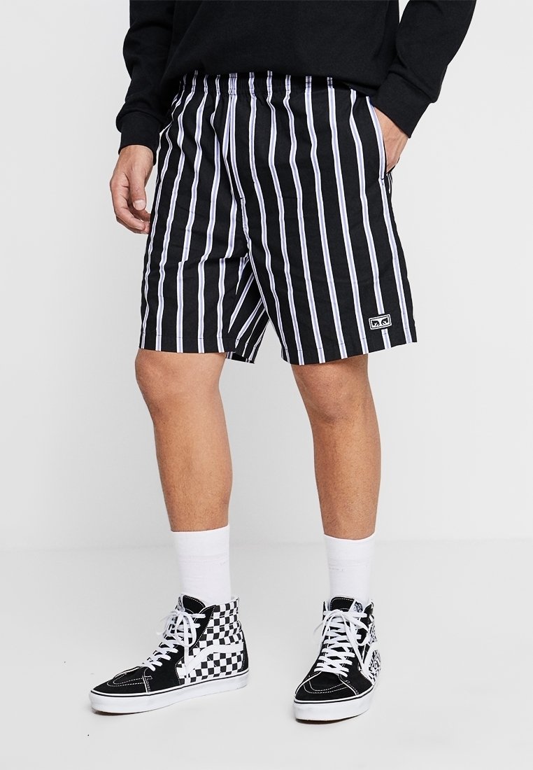 Czarno-białe krótkie spodenki w paski z elastycznym pasem; zestawione z wysokimi trampkami w kratę i białymi skarpetkami.