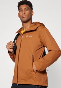 Brown waterproof jacket with a hood, zippered front, and side pockets. Features an orange zipper and accents, made from smooth, durable material.