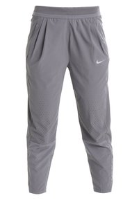 Pantalon de sport gris avec ceinture élastique, poches latérales, ventilation perforée sur les cuisses et logo Nike blanc sur le côté gauche.