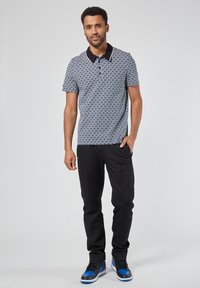 Lyhythihainen polo-paita, jossa on geometrinen sininen kuvio, musta kaulus, yhdistetty mustiin housuihin ja sinivalkoisiin tennareihin.