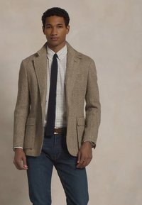 Blazer houndstooth in lana marrone e beige, abbinato a una camicia a quadri bianca e blu, jeans blu scuro e una cravatta blu navy.