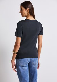 T-shirt noir à manches courtes avec un col rond, au design ajusté et à la texture lisse, associé à un jean bleu clair ; vu de dos.