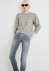 Pull en maille gris clair avec un motif texturé, associé à un jean bleu délavé slim fit et des lunettes de soleil noires.