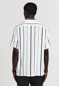 Weißes Kurzarmhemd mit schwarzen vertikalen Streifen, ausgestattet mit einem lockeren Kragen und strukturiertem Stoff. Die Rückansicht zeigt ein schlichtes Design.
