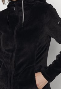 Black fleece jacket with a zippered front, hood, and two side pockets. Features textured material and contrasting drawstring accents.