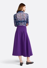 Transparante bloemenblouse met een gerimpelde kraag, gecombineerd met een paarse A-lijn midi rok. Bruine platte schoenen, zichtbare enkel tatoeage.