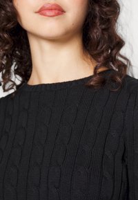 Černý pletený svetr s copánkovým vzorem, kulatým výstřihem a žebrovanými lemovkami. Látka má měkký, strukturovaný vzhled.