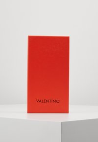 Crveni pravokutni kutija s sjajnom završnom obradom. Ime branda "VALENTINO" prikazano je crnim slovima na dnu. Minimalistički dizajn.