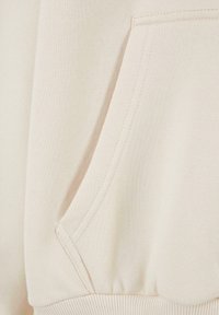 Beige Sweatshirt mit Kängurutasche, geripptem Saum und glatter Textur. Dezente Stickereidetails entlang der Taschenkanten.