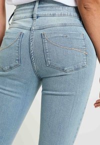 Jeans de tiro alto en azul claro, hechos de denim, con bolsillos traseros con costuras curvadas y sutiles acentos de costura metálica.