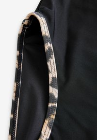 Svart tyg med en slät textur, med en leopardmönstrad kant längs kanterna och kontrasterande sömmar.