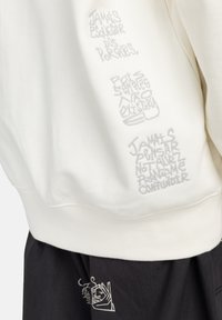 Cream sweatshirt with embroidered text in gray on the left sleeve, paired with black bottoms featuring white graphic accents.