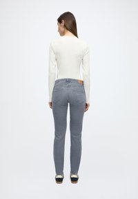 Kitsad heledat halli värvi teksapüksid, valmistatud teksariidest, keskmise kõrgusega vööjoonega, kahe tagataskuga, vööpaelal nahast plaadiga ja kergelt pleekinud pesuga.