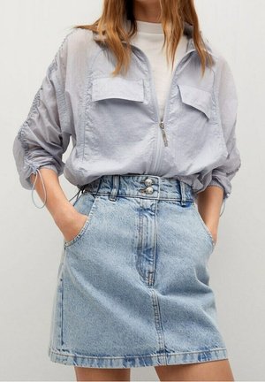 Jasnoszara kurtka na zamek błyskawiczny z dwoma kieszeniami na piersi, zestawiona z jasnoniebieską spódnicą jeansową z wysokim stanem, zapinaną na guziki z kieszeniami.