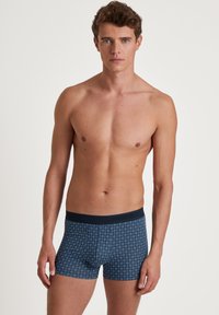 Marineblauwe boxershorts met een diamanten patroon, gemaakt van zacht materiaal. Heeft een donkere tailleband met merkletters. Standaard pasvorm en lengte.