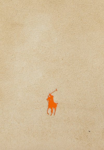 Beigen pehmeä mokkanahka, jossa on sileä pinta ja näkyvä oranssi poloilijan logo vasemmassa alakulmassa.